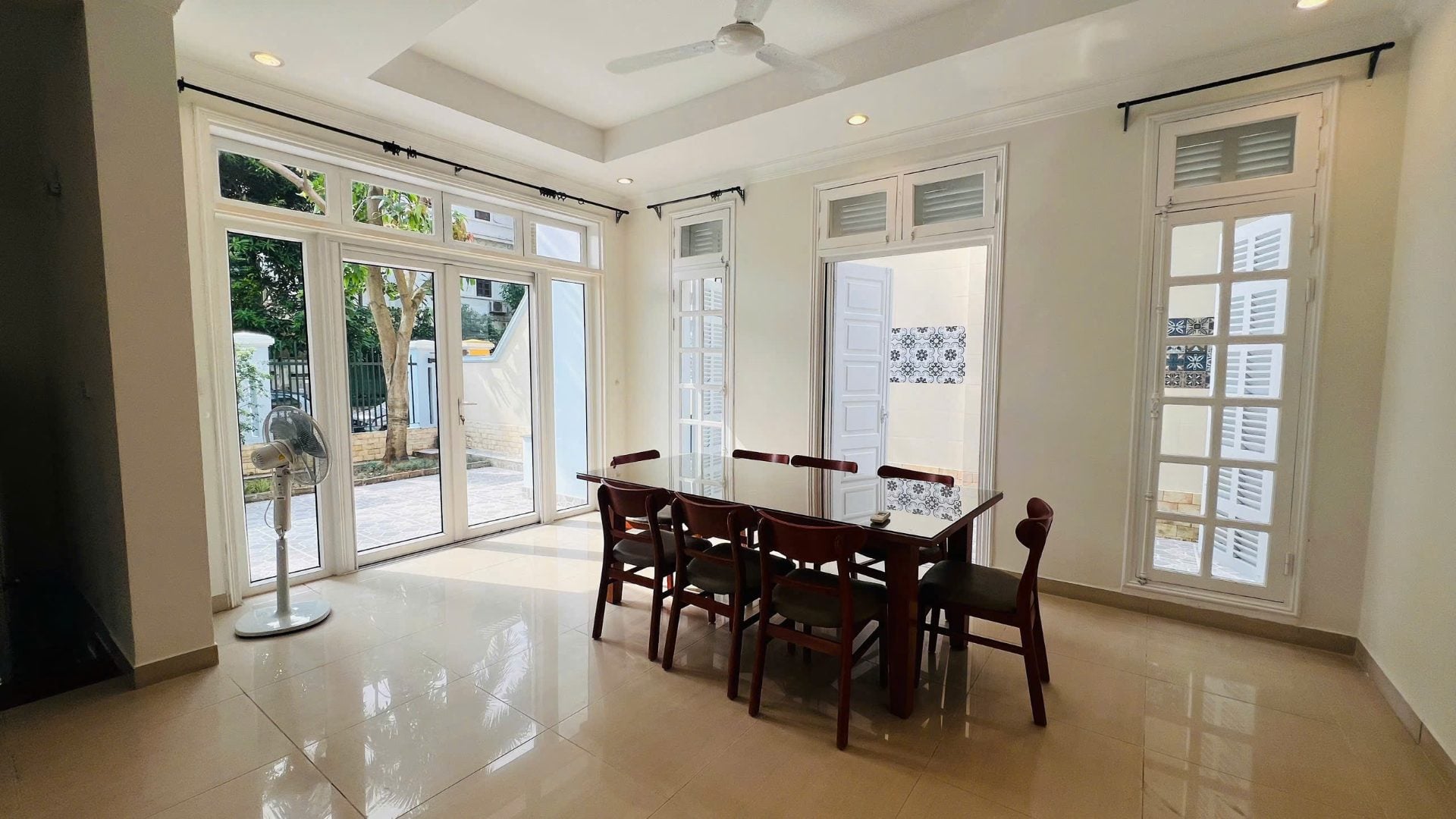 A bright dining room with a long wooden table and French doors opening onto a paved patio