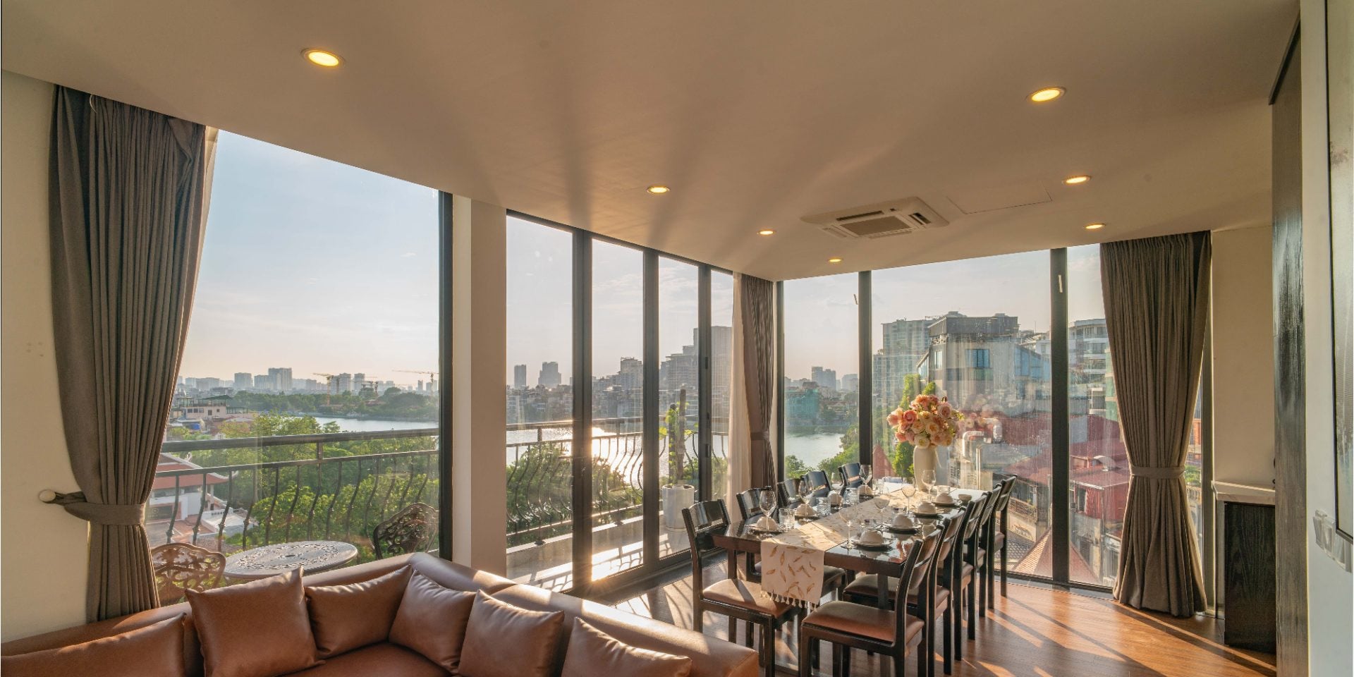 Corner living and dining room with floor-to-ceiling windows looking over West Lake, trees and the city skyline at golden hour