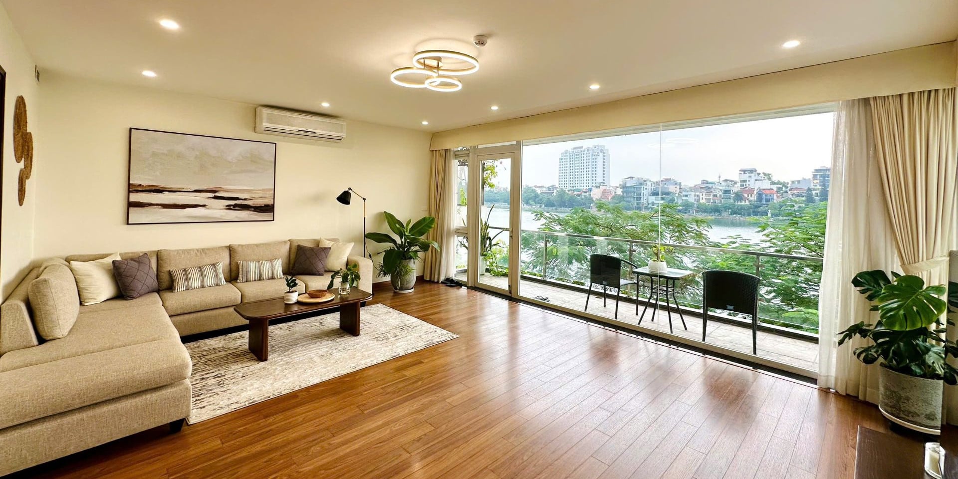 Living room with a sofa and a glass wall opening onto a balcony, with West Lake and the skyline beyond