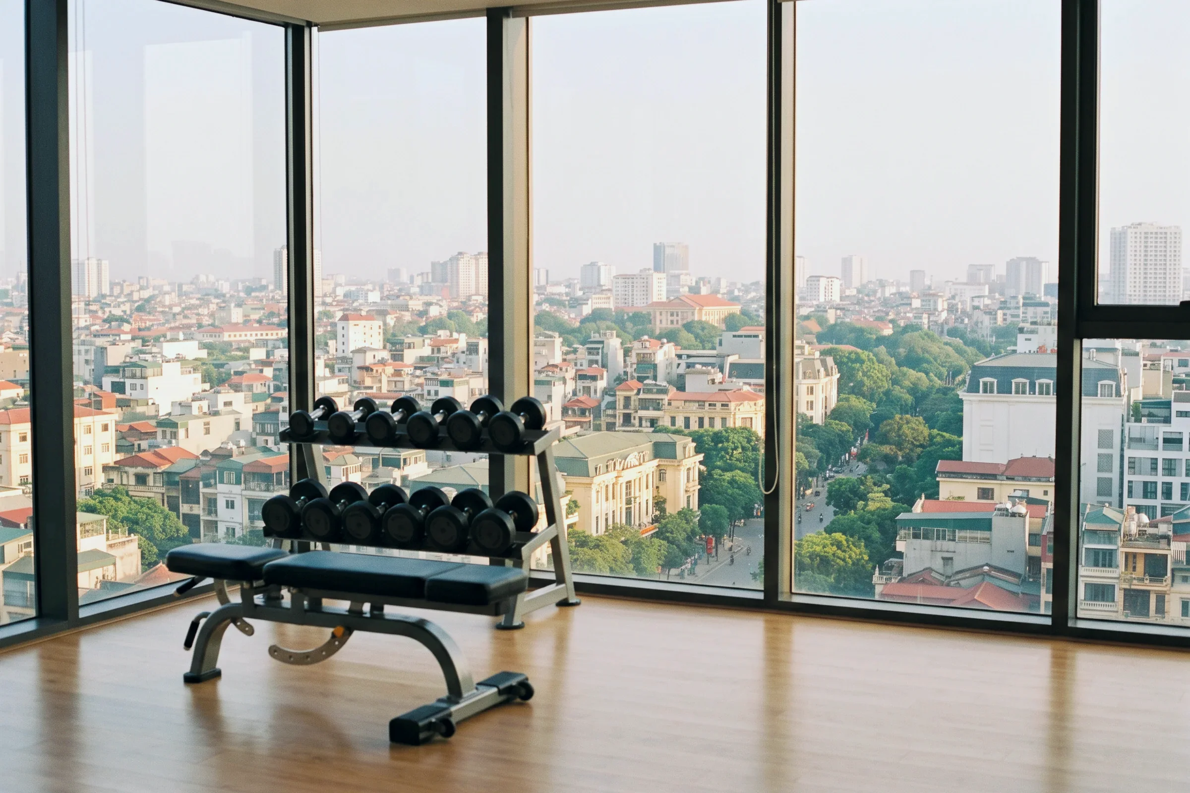 An empty gym with dumbbells by tall windows over the city