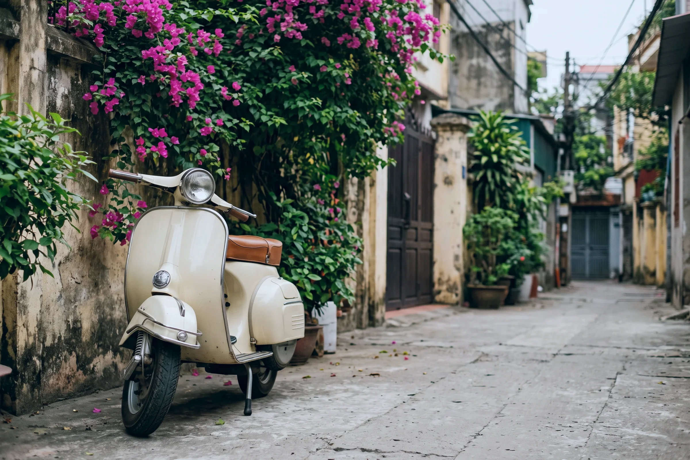 A cream scooter parked in a quiet lane under bougainvillea