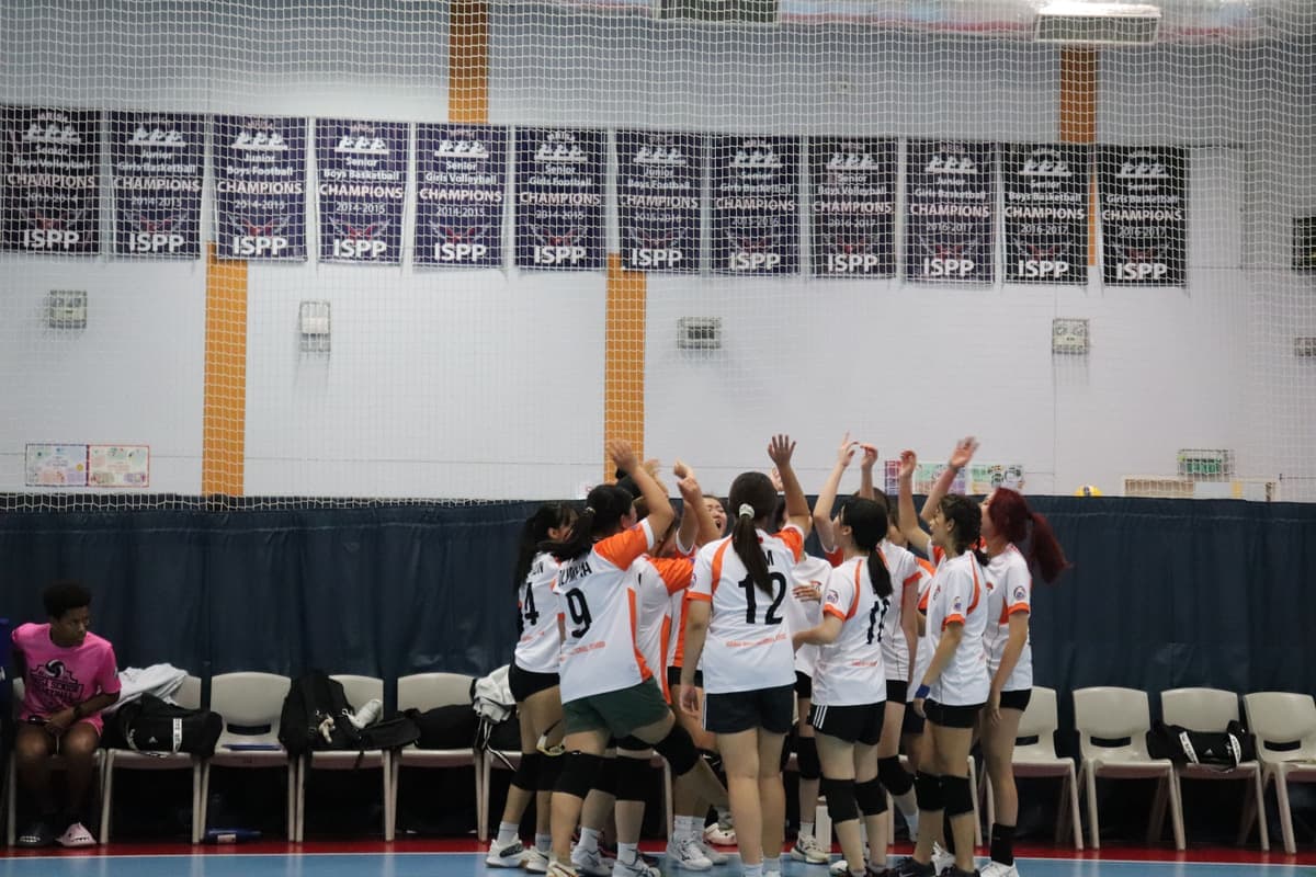 The Hanoi International School girls' volleyball team celebrating together at a tournament