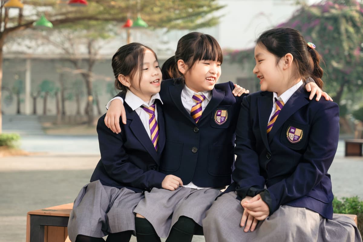 Three primary students in school blazers sitting together outdoors at The Olympia Schools