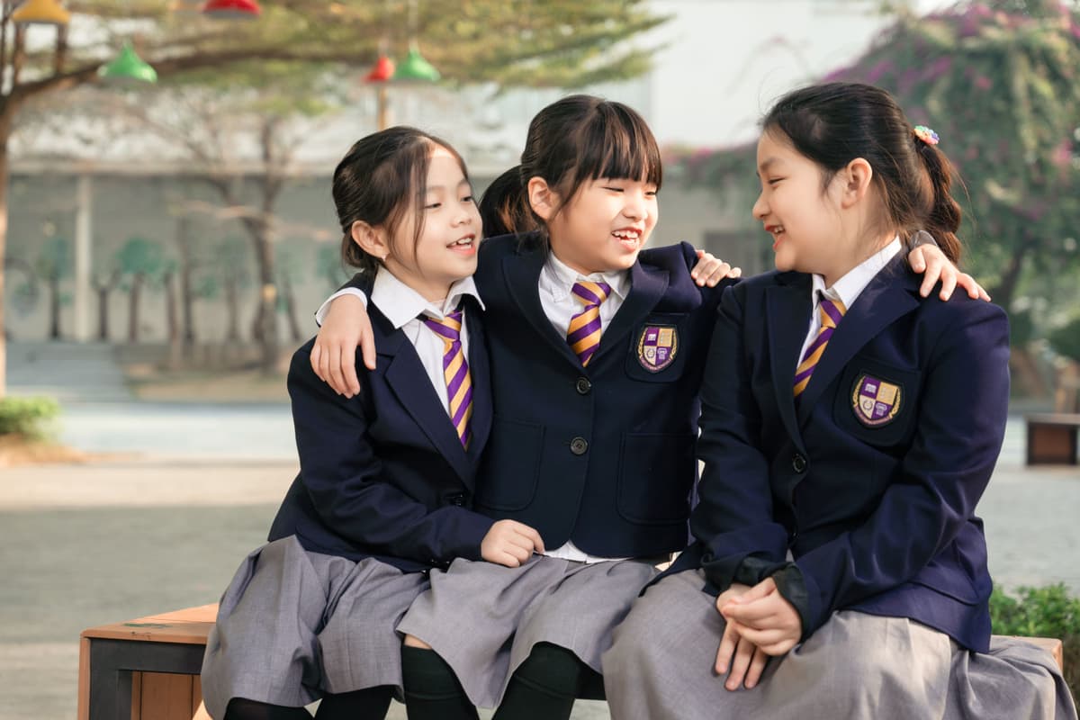 Three primary students in school blazers sitting together outdoors at The Olympia Schools